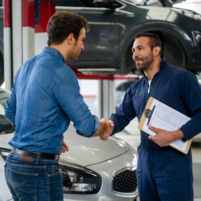 Latin American man greeting a mechanic with a handshake while picking up his car at an auto repair shop